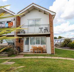 A two story house with a balcony and outdoor chairs and table at 63 The Waterside Holiday Park in Corton
