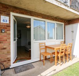 An outdoor patio area with a wooden table and four chairs next to a glass door at 63 The Waterside Holiday Park in Corton