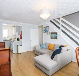 A living room with a gray corner sofa with cushions under stairs and a kitchen visible through a doorway at 63 The Waterside Holiday Park in Corton