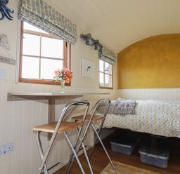A small bedroom with a bed a table with two chairs two windows and a yellow accent wall at Dot May Porteath near Polzeath