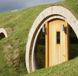 A wooden door with a small window built into a grassy hill with two silver wall lights
