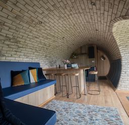 An arched brick room with a blue bench with cushions a wooden kitchen island with stools and a round door at Badgers View in Rhayader