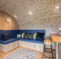 A corner seating area with blue cushions and pillows next to a wooden breakfast bar with stools at Badgers View in Rhayader