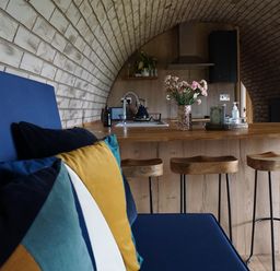 A kitchen with a wooden island and stools with a blue sofa and colorful cushions in a space with a curved brick ceiling at Badgers View in Rhayader