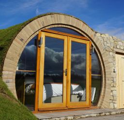 A circular wooden door with glass panels built into a grassy hillside at Hares View in Rhayader