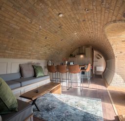 A curved brick interior with a seating area a wooden coffee table chairs and a kitchen at Hares View in Rhayader