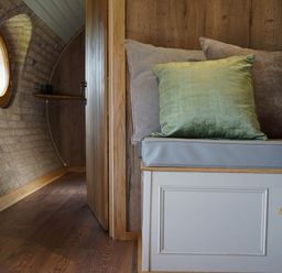 A small seating area with cushions beside a doorway in a wooden interior with a round window at Hares View in Rhayader