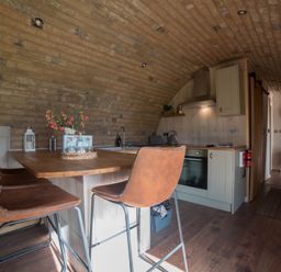 A kitchen area with a wooden island and brown chairs under a curved brick ceiling at Hares View in Rhayader