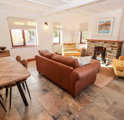 A living room with a brown sofa yellow armchairs a wooden dining table and a stone fireplace at Fountain Folly in Moylgrove near St Dogmaels