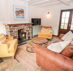 A living room with a stone fireplace two yellow armchairs a brown sofa a rug and a TV cabinet at Fountain Folly in Moylgrove near St Dogmaels