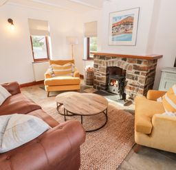A living room with a brown sofa yellow armchairs stone fireplace and round wooden coffee tables at Fountain Folly in Moylgrove near St Dogmaels