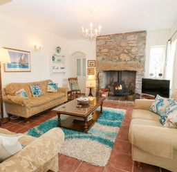 A living room with three sofas a wooden coffee table a stone fireplace and a television at Gorphwysfa in Llanddona near Beaumaris