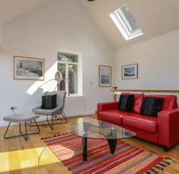 A living room with a red sofa black cushions a gray chair with a footrest and glass coffee table at Gorphwysfa in Llanddona near Beaumaris