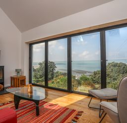 A living room with large windows overlooking a coastal view fireplace glass coffee table and red rug at Gorphwysfa in Llanddona near Beaumaris