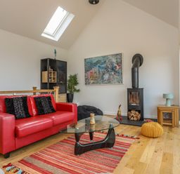 A living room with a red sofa black cushions a glass coffee table a fireplace and a skylight at Gorphwysfa in Llanddona near Beaumaris