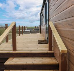 A wooden deck with glass railing and outdoor seating at Sandy Bay Retreat in Hasguard Cross near Broad Haven
