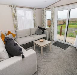 A living room with a sectional sofa and pillows next to sliding glass doors at Sandy Bay Retreat in Hasguard Cross near Broad Haven