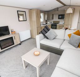 A living room with a gray sofa and cushions a small table with a bowl a TV on a wooden stand and a kitchen in the background at Sandy Bay Retreat in Hasguard Cross near Broad Haven