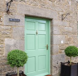 A green door set in a stone wall with two potted topiary bushes on either side at The Granary in Longwitton near Morpeth