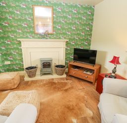 A living room with patterned wallpaper a television on a wooden stand and a light grey armchair at The Granary in Longwitton near Morpeth
