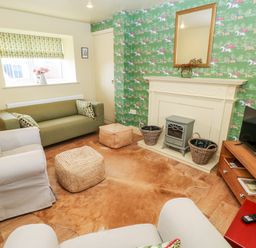 A living room with green wallpaper a fireplace and a television at The Granary in Longwitton near Morpeth