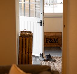An open white door with rubber boots on a rug and a wicker basket in a hallway at The Lodge in Newby Bridge