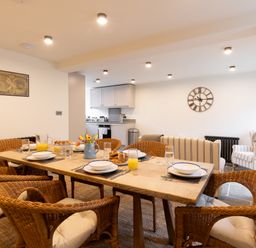 A dining area with a wooden table set with dishes and wicker chairs in an open plan kitchen and living space at The Lodge in Newby Bridge