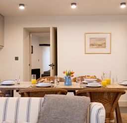 A dining room with a wooden table set with plates glasses jug of orange juice and a vase with flowers at The Lodge in Newby Bridge