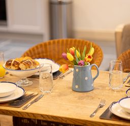 A dining table with bowls plates glasses of water and orange juice bread and a vase with tulips at The Lodge in Newby Bridge