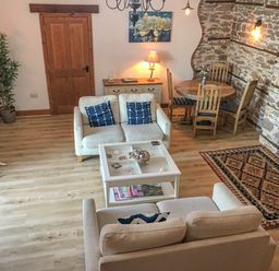 A living room with two beige sofas a white coffee table a wooden dining table with four chairs and a stone wall at Baronet's Quarters in Lynton