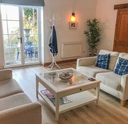 A living room with two beige sofas a glass coffee table and a coat stand near a glass door at Baronet's Quarters in Lynton