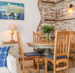 A dining area with a round wooden table and four chairs with cushions next to a stone wall and a painting at Baronet's Quarters in Lynton