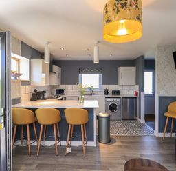A kitchen with a breakfast bar and yellow stools next to a living area with a mounted TV at Eala Bhan Cottage in Clachan near Balivanich