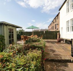 A backyard with a green storage shed wooden patio furniture with an umbrella and a metal chiminea at Abbey Farm House in St Bees