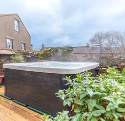 An outdoor hot tub on a wooden deck next to a stone wall with plants at Abbey Farm House in St Bees
