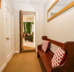 A hallway with a wooden bench and red heart cushions a mirror on the wall and a doorway leading to a room with chairs at Abbey Farm House in St Bees