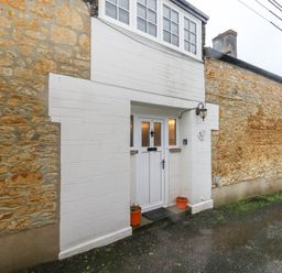 A stone exterior wall with a white entrance door and two small plant pots at Poppy Cottage in Beaminster