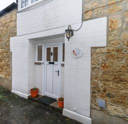 A white door with windows and flower pots beside it set in a stone wall at Poppy Cottage in Beaminster