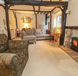 A living room with sofas wood beam ceiling a fireplace and tables at Poppy Cottage in Beaminster