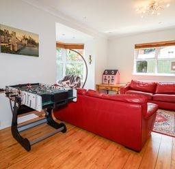 A living room with red leather sofas a foosball table and a dollhouse on a wooden table at Trem Y Don in Dolgarrog
