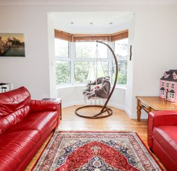 A living room with two red leather sofas a hanging chair by a bay window a wooden table with a pink dollhouse and a patterned rug on the floor at Trem Y Don Dolgarrog