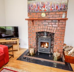 A living room with a brick fireplace with a wood-burning stove and firewood at Trem Y Don in Dolgarrog