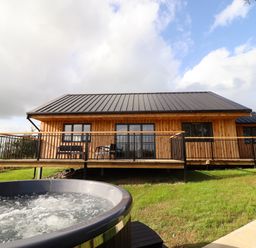 A wooden lodge with a metal roof and a deck overlooking a grassy area with a hot tub at Mynydd Y Glyn Lodge in Llanfyllin near Llanrhaeadr-Ym-Mochnant