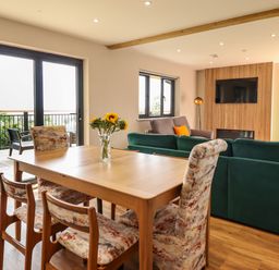 A dining table with chairs and a vase of sunflowers next to a living area with sofas a TV and large windows at Mynydd Y Glyn Lodge in Llanfyllin near Llanrhaeadr-Ym-Mochnant