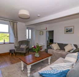 A living room with sofas, cushions, armchair, coffee table with flowers, window with curtains and door at Towyn Hall in New Quay