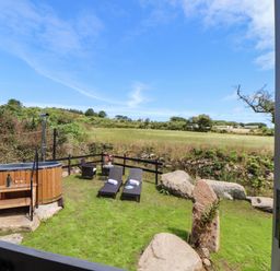 A garden area with two lounge chairs towels a wooden hot tub and a small table with chairs at Bosulla Shepherds Hut in Penzance