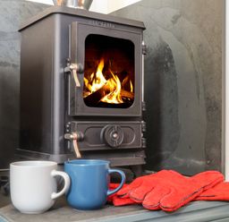 Wood burning stove with fire two mugs and red gloves in front at Bosulla Shepherds Hut in Penzance