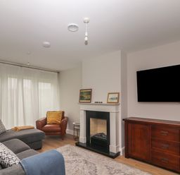 A living room with grey sofa and armchair near a fireplace and a wall mounted television at 19A Lighthouse Village in Fenit County Kerry