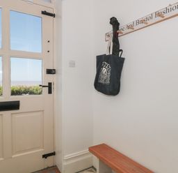 A corner entryway with a wooden bench a wall-mounted coat rack holding bags and an umbrella and a door with glass panels at 49 Esplanade in Burnham-On-Sea