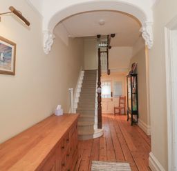 A hallway with wooden floorboards a staircase a wooden cabinet a framed picture and a glass display case at 49 Esplanade in Burnham-On-Sea